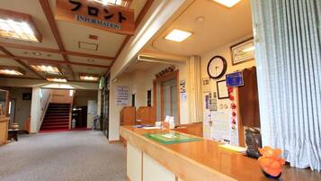 A reception area with a wooden reception desk, a clock, and a bulletin board with various notices.
