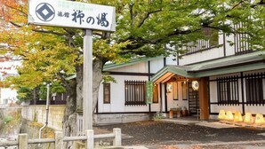 A traditional Japanese building with a signboard, a wooden fence, and a tree with autumn leaves. - Yanaginoyu Hotel (Aomori)