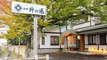A traditional Japanese building with a signboard, a wooden fence, and a tree with autumn leaves.