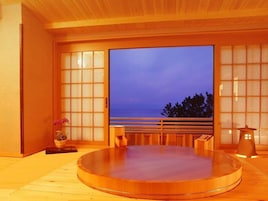 Un onsen japonés tradicional con interior de madera, un amplio ventanal con vistas al mar y una pequeña mesa de madera.