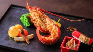 Un langostino sobre una bandeja negra con dos objetos redondos y un recipiente rojo.
