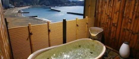 A wooden room with a bathtub and a view of a beach and mountains.