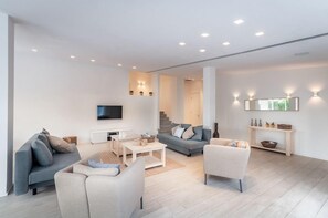 Una sala de estar moderna con un televisor de pantalla plana, sofás, una mesa de centro y una escalera que lleva a otra habitación.
