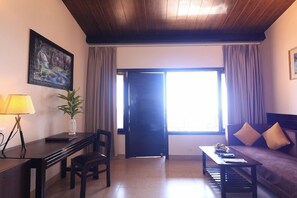 A room with a wooden ceiling, a desk with a lamp, a chair, a sofa, and a large window with curtains. - Ecko Kasang Regency (Lansdowne)