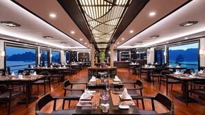 A restaurant with tables set for dining, large windows offering views of the sea, and a central bar area. - Peony Cruises (Hai Phong)