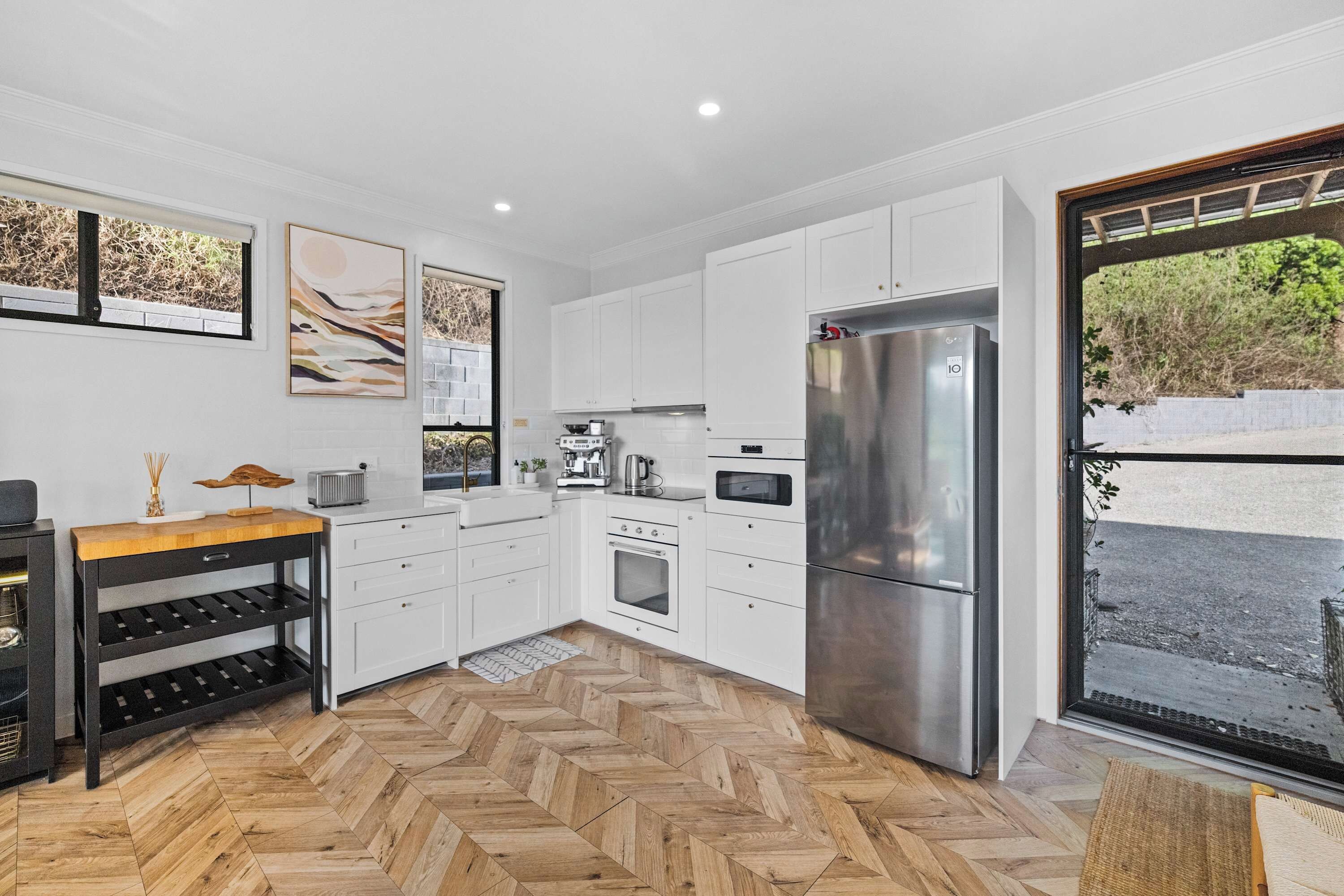 Una cocina moderna con armarios blancos, un refrigerador de acero inoxidable y un piso de madera en patrón de espiga.