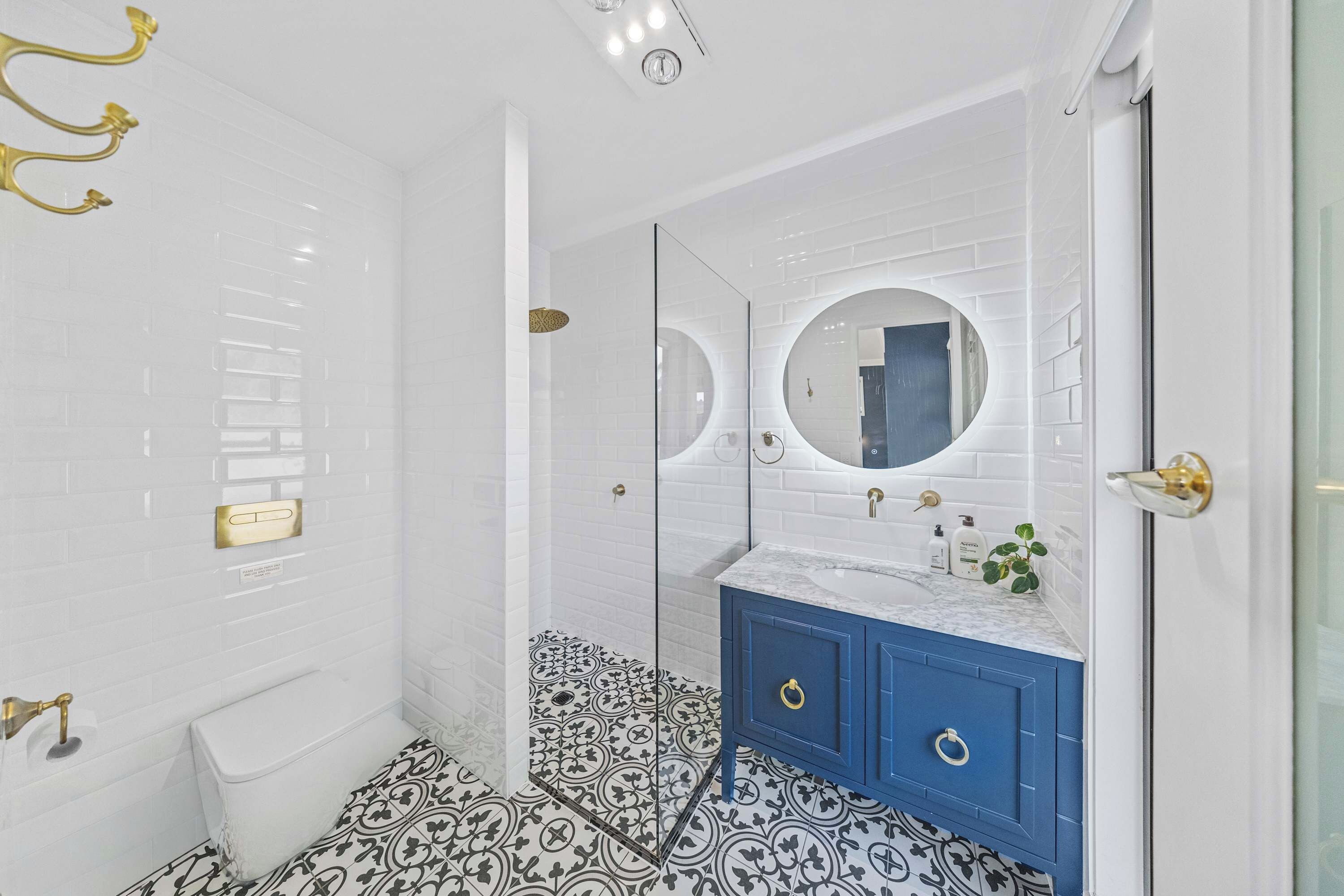 Un bagno con piastrelle bianche tipo metro, un mobile lavabo blu, uno specchio rotondo e un pavimento decorato.