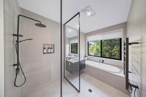 Een moderne badkamer met een douchecabine, een groot raam met uitzicht op groen en een wastafel met een bad.