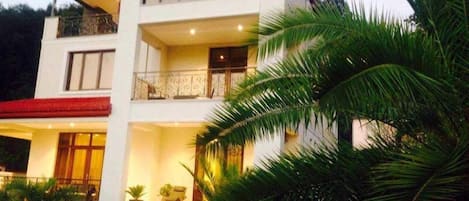 Un edificio de varios pisos con balcones, una entrada cubierta y un jardín ajardinado con palmeras.