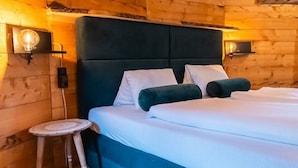 A wooden cabin-style room with a bed, two wall-mounted light fixtures, and a small wooden stool.