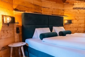 Quarto de cabana de madeira com cama, duas luminárias fixadas na parede e uma pequena mesa redonda.