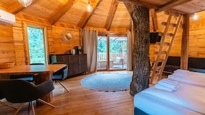 A wooden cabin interior with a dining table, chairs, a bed, and a ladder.