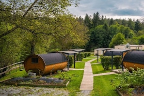 A row of cylindrical wooden cabins with attached roofs, arranged in a row with a paved walkway between them.