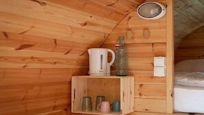 A wooden interior with a shelf holding a white kettle, a green bottle, and several mugs.