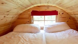 A single bed with a red valance in a wooden room with a sloped ceiling.