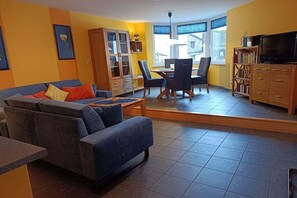 A living room with a sofa, dining table, chairs, a cabinet, and a television. - Holiday home with 1 bedroom (St. Aldegund)