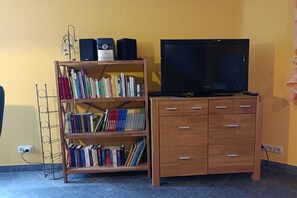 A room with a wooden bookshelf filled with books, a television on a wooden cabinet, and a wall socket. - Holiday home with 1 bedroom (St. Aldegund)