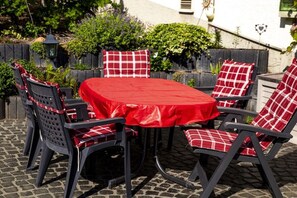Une terrasse extérieure avec une table ronde et des chaises, entourée d’un jardin et d’un mur blanc.