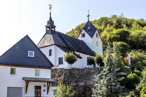 A traditional building with a stone wall and a steeply pitched roof, surrounded by lush greenery. - Holiday home with 1 bedroom (St. Aldegund)
