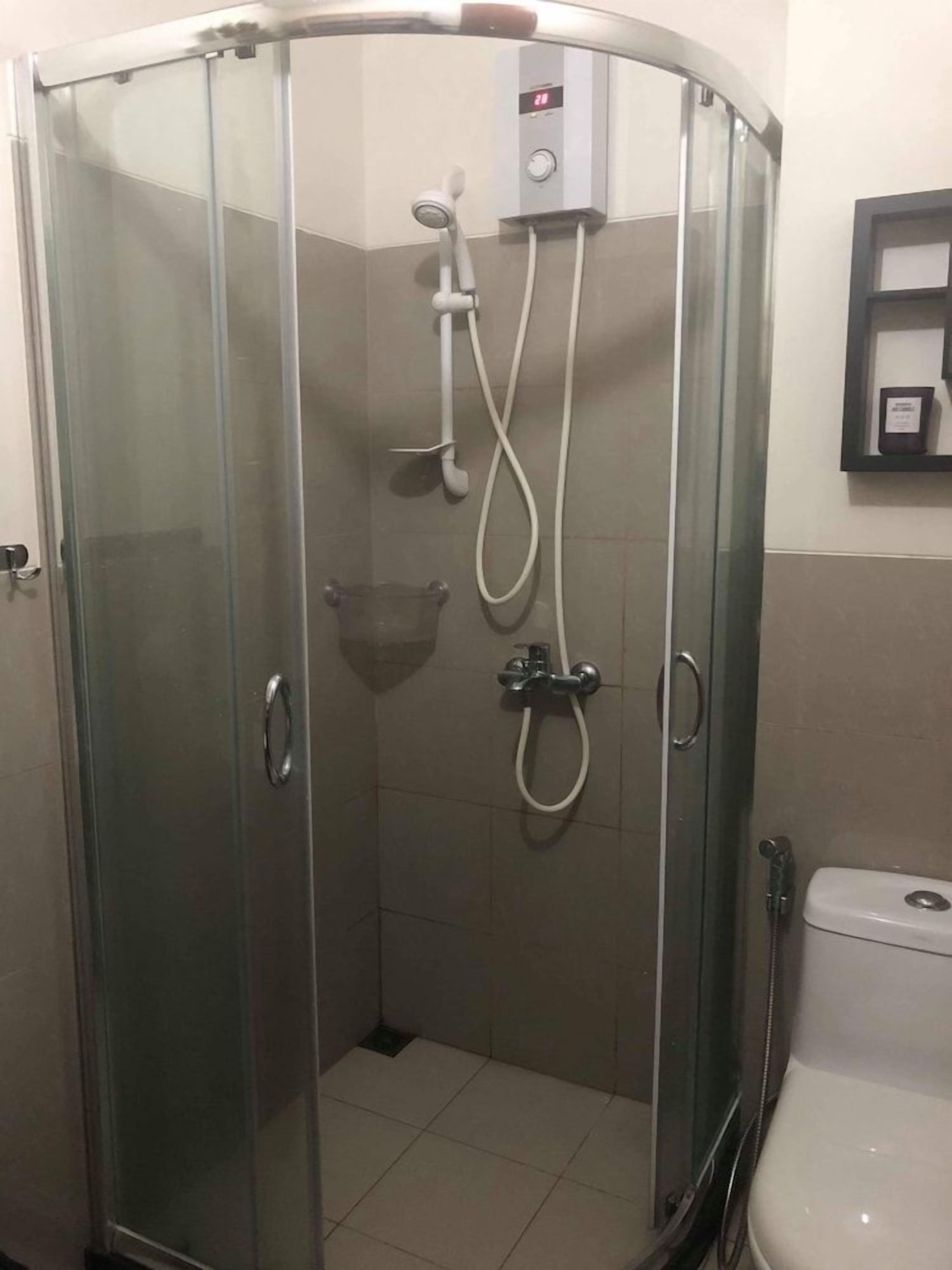 A glass-enclosed shower stall with a handheld showerhead and a wall-mounted control panel.
