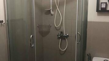 A glass-enclosed shower stall with a handheld showerhead and a wall-mounted control panel.