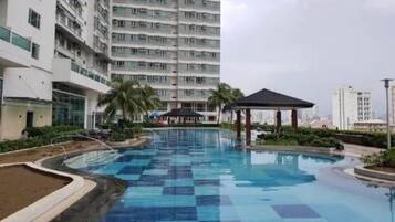 A swimming pool with a checkered pattern, surrounded by greenery and a tall building in the background.