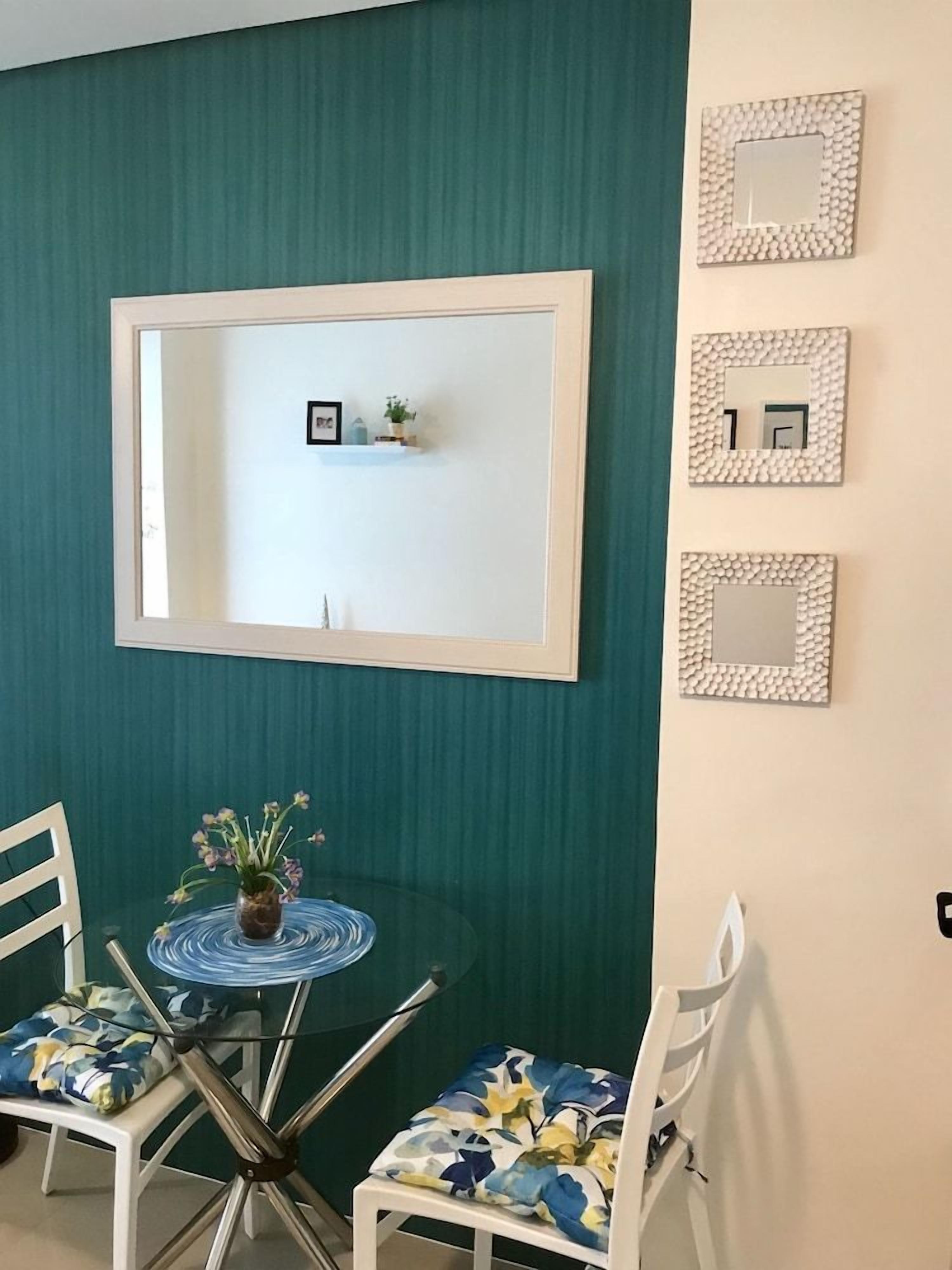 A room with teal walls, a white-framed mirror, a small shelf with decorative items, and a round table with chairs.