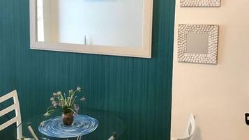 A room with teal walls, a white-framed mirror, a small shelf with decorative items, and a round table with chairs.