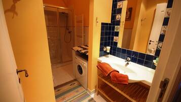 Un bagno compatto con doccia, lavatrice e lavandino con porta asciugamani.