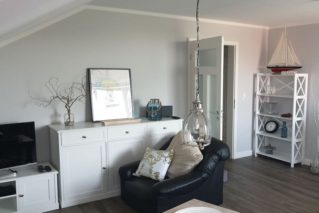 A living room with a black leather sofa, a white cabinet, a television, and a decorative sailboat shelf.