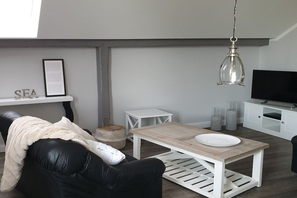Ein modernes Wohnzimmer mit einem schwarzen Ledersofa, einem Holztisch, einer weißen TV-Konsole und einer Pendelleuchte.