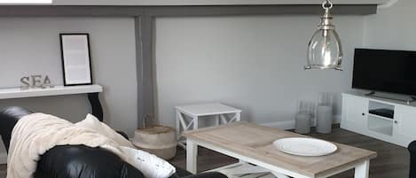 Una sala de estar moderna con un sofá de cuero negro, una mesa de centro de madera, un mueble blanco para la TV y una lámpara colgante.