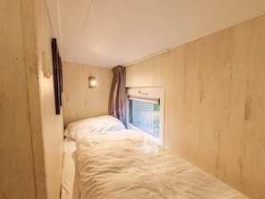 Ein schmales Zimmer mit einem Einzelbett, einem Fenster mit Vorhängen und einer Wandleuchte.