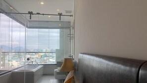 A modern bathroom with a glass shower enclosure, a bathtub, and a seating area with a view of the city. - La Maison De Hang (Da Nang Municipality)