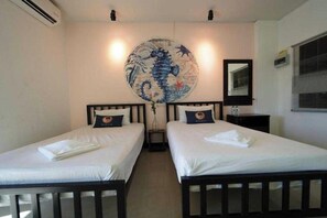 Une chambre avec deux lits, une tapisserie ronde au mur, un miroir et une fenêtre avec des stores.