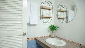 A bathroom with a white sink, two wall-mounted mirrors, a towel rack, and a small potted plant.