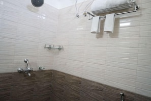 A bathroom with white tiled walls, a showerhead, a towel rack with two towels, and a glass shelf. - Treebo Hotel Pemaling (Guwahati)