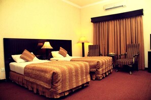 Ein Hotelzimmer mit zwei Betten, einem Schreibtisch, einem Stuhl und einem großen Fenster mit Vorhängen.