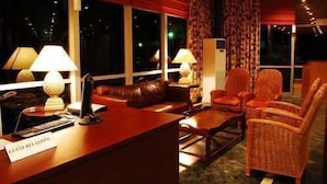 Habitació d'hotel amb taulell de recepció, un sofà de cuir, dues cadires de vimet i una finestra amb cortines.