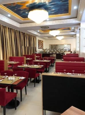 Un restaurant amb seients de vellut vermell, taules i un sostre amb un mural pintat, i un penjall.