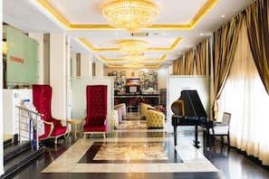 Un rebedor espaiós amb un piano, seients vermells i daurats, i una zona de bar.