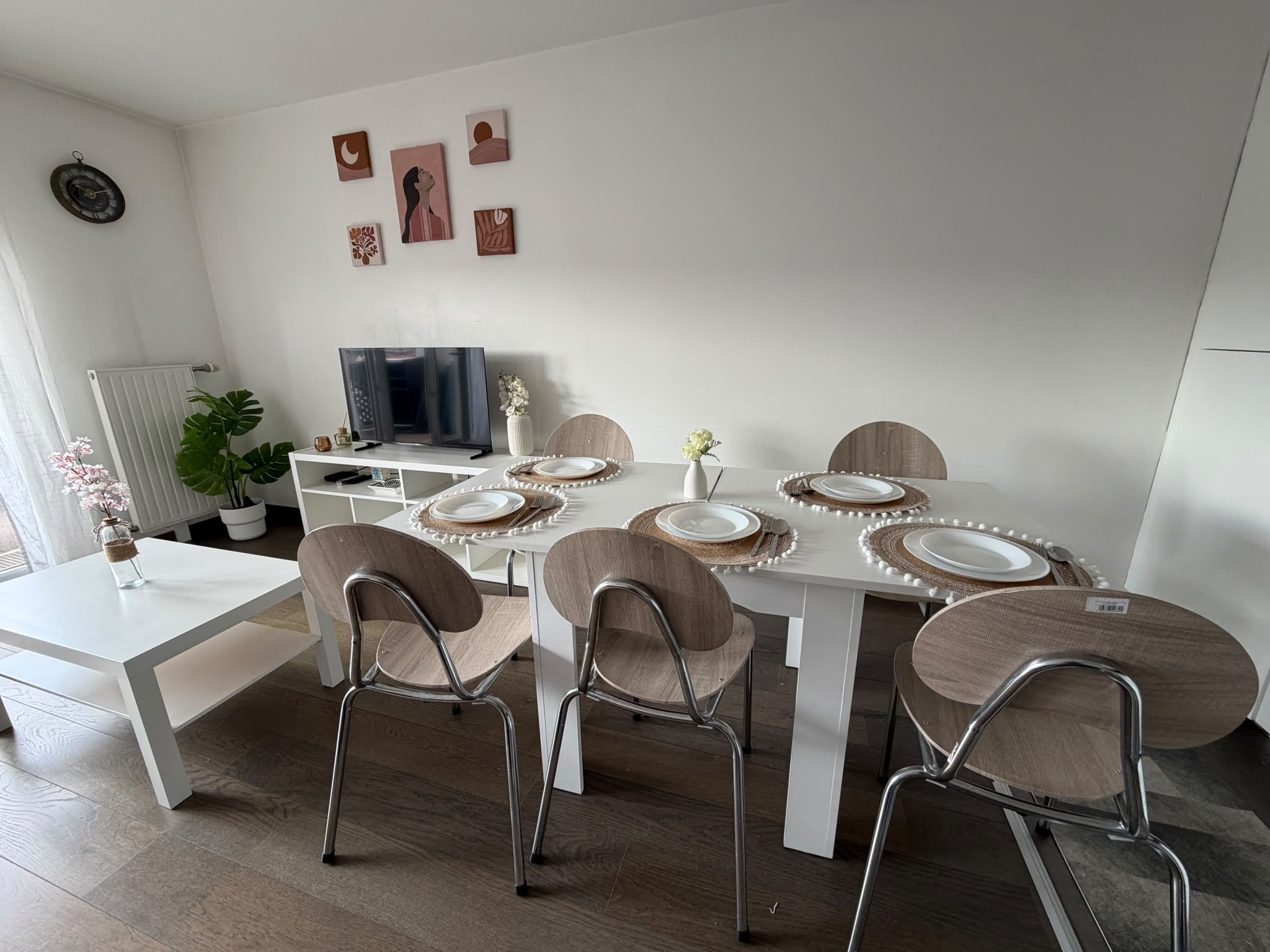 Un espace repas moderne avec une table blanche dressée pour quatre personnes, entourée de chaises en bois à structure métallique.