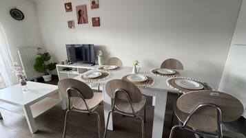 Un espace repas moderne avec une table blanche dressée pour quatre personnes, entourée de chaises en bois à structure métallique.