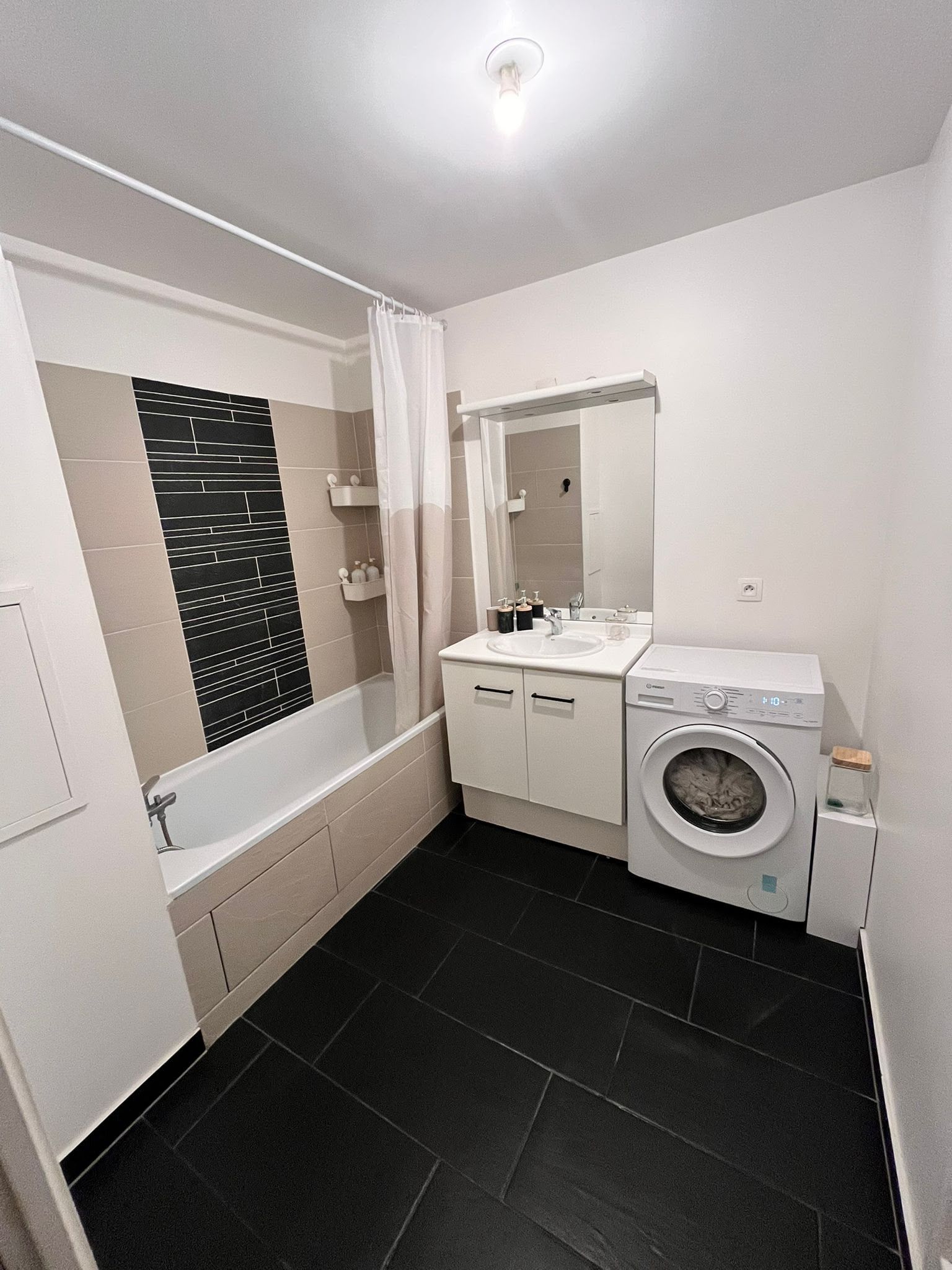 A modern bathroom with a bathtub, a sink, a mirror, and a washing machine.