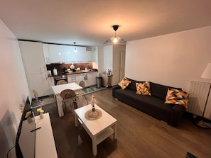 A compact living space with a dining area, a sofa with patterned cushions, and a kitchen in the background. - L'Escale Parisienne: a perfect 2-bedroom apartment in charming Tremblay (Tremblay-en-France)