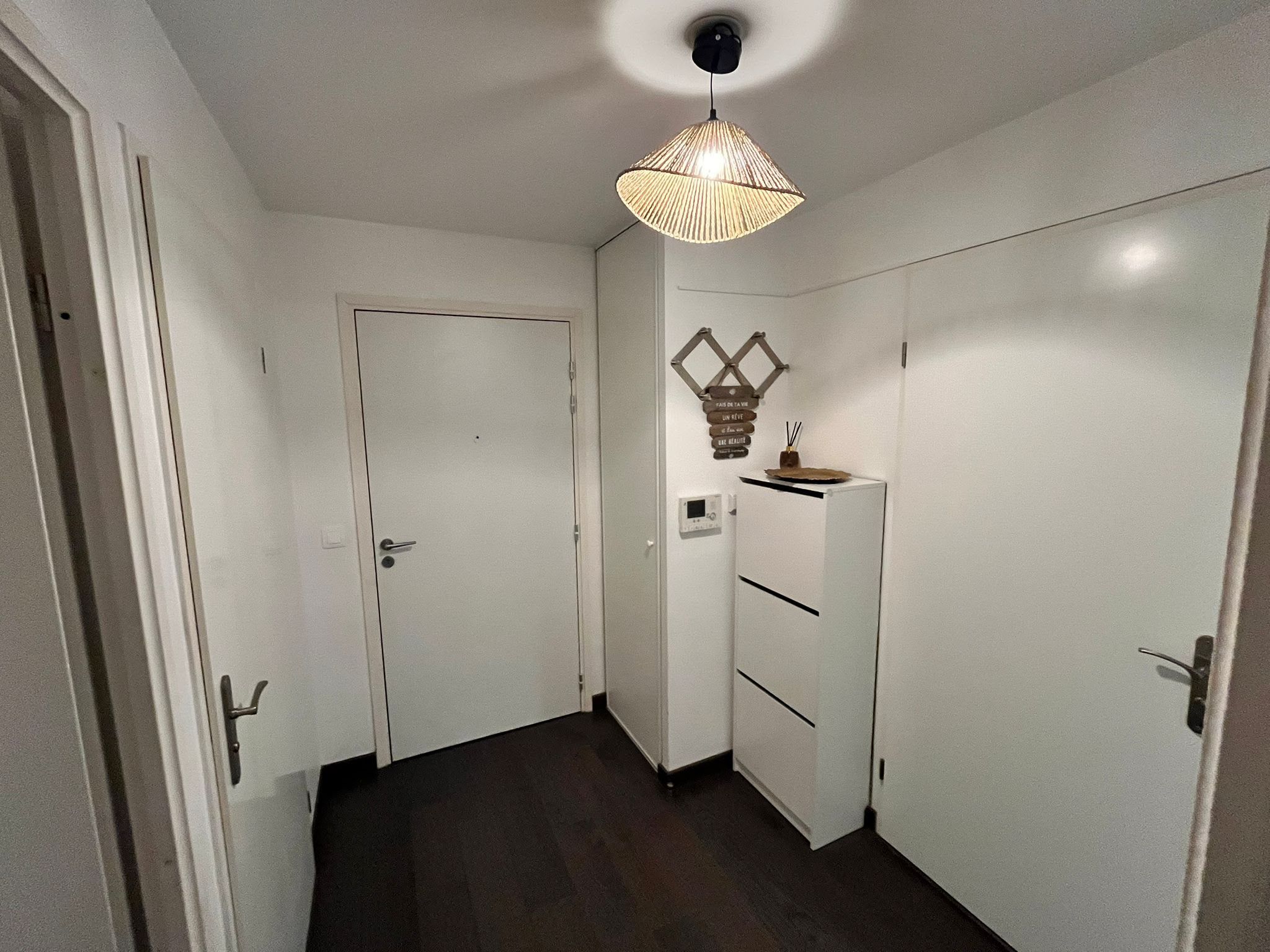 Un couloir avec une porte blanche, une armoire blanche et un luminaire suspendu.