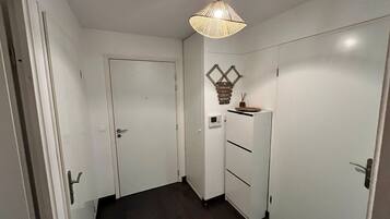 Un couloir avec une porte blanche, une armoire blanche et un luminaire suspendu.