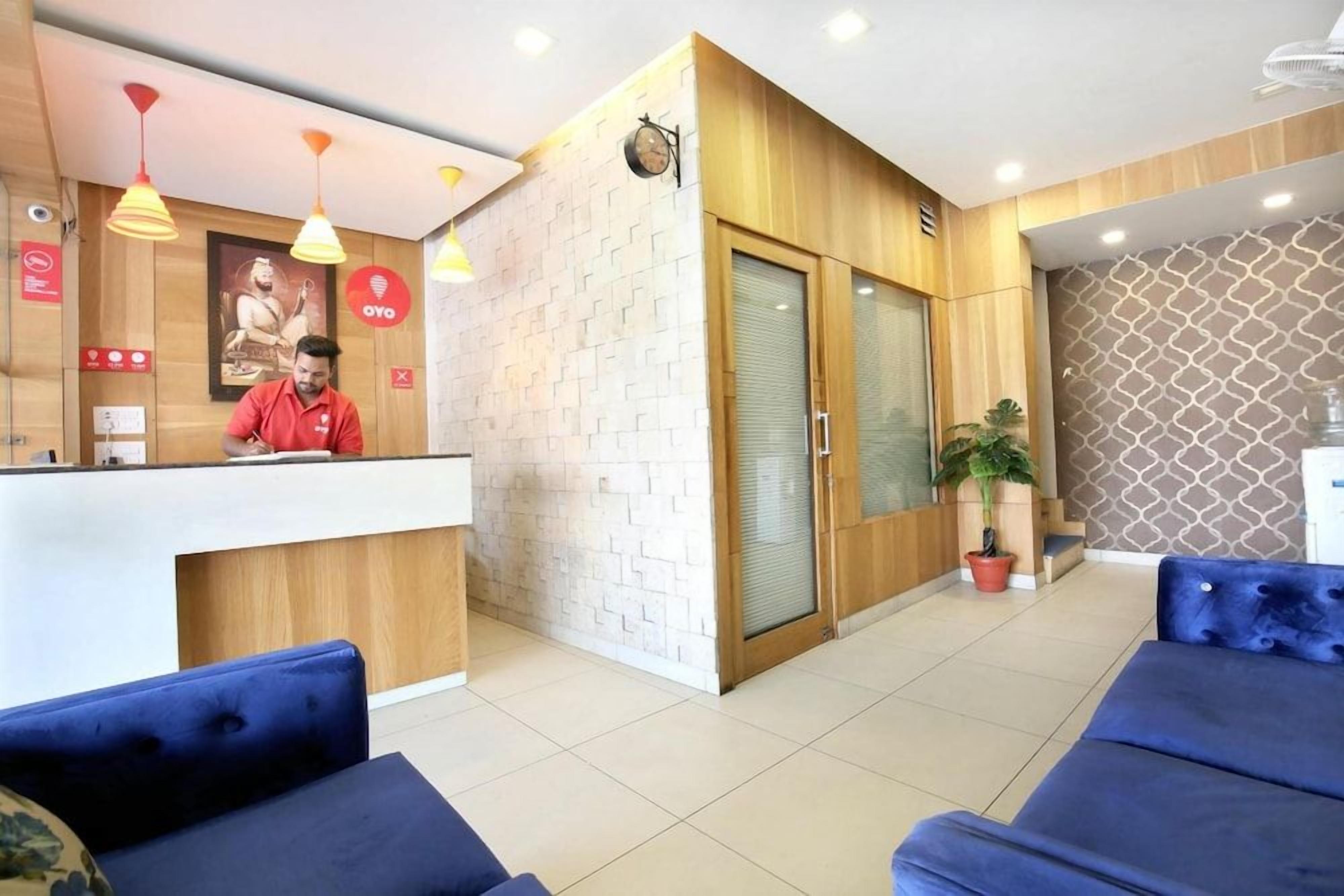 A hotel reception area with a wooden reception desk, a receptionist, and blue seating.