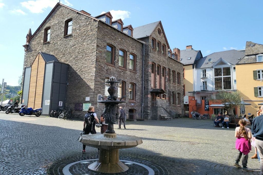 A stone building with a fountain in the center of a cobblestone square.