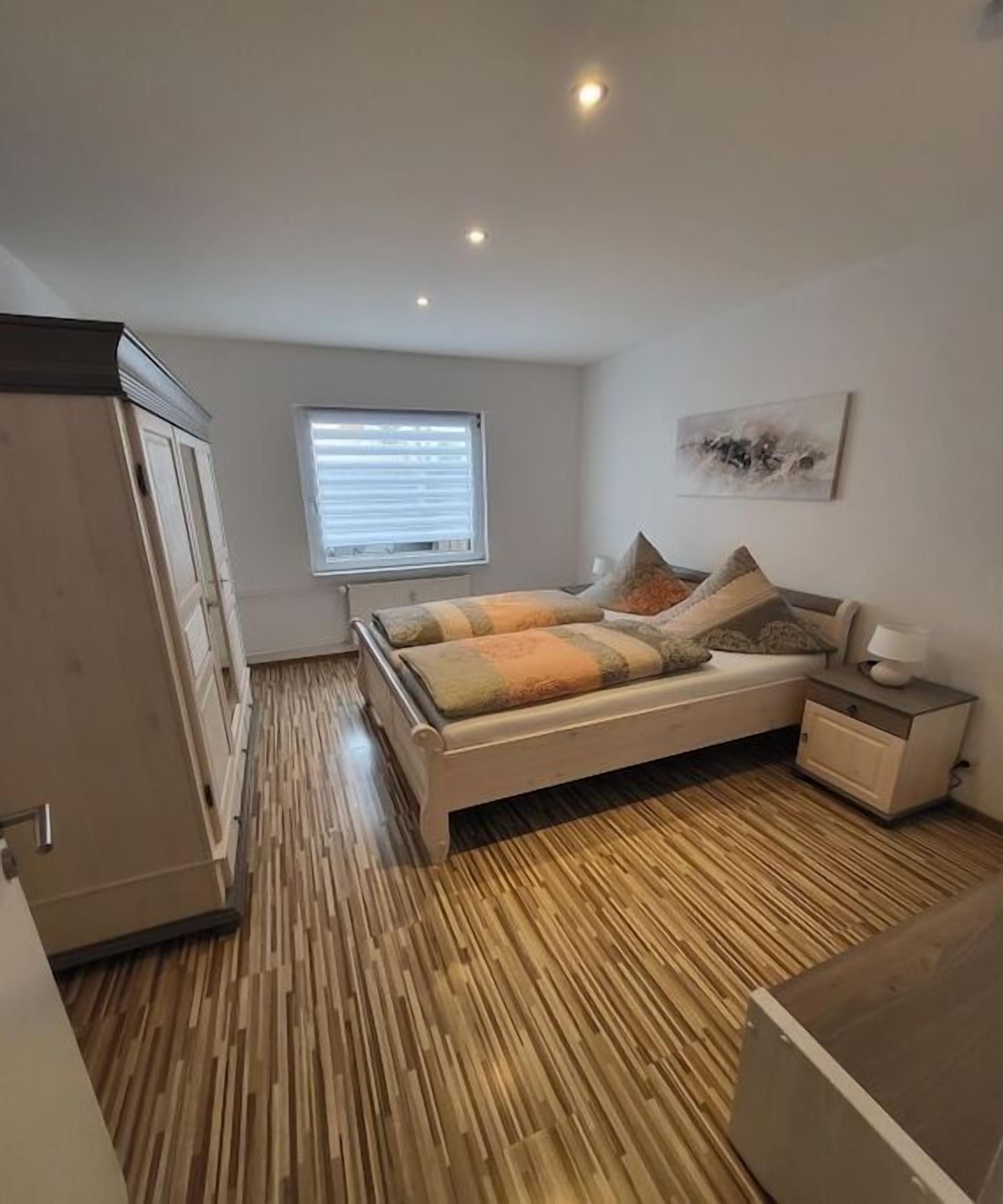 A bedroom with a bed, bedside table, window, and wooden flooring.